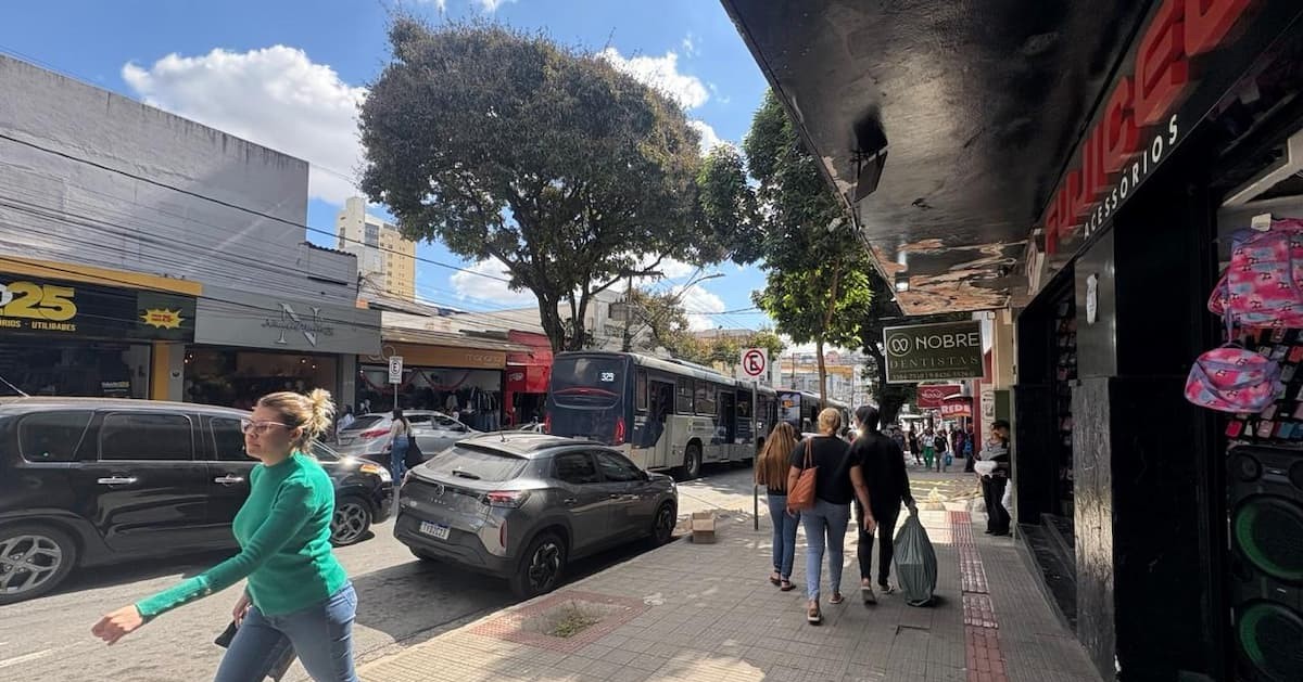 Pessoas caminhando pela calçada em uma rua comercial movimentada durante o dia