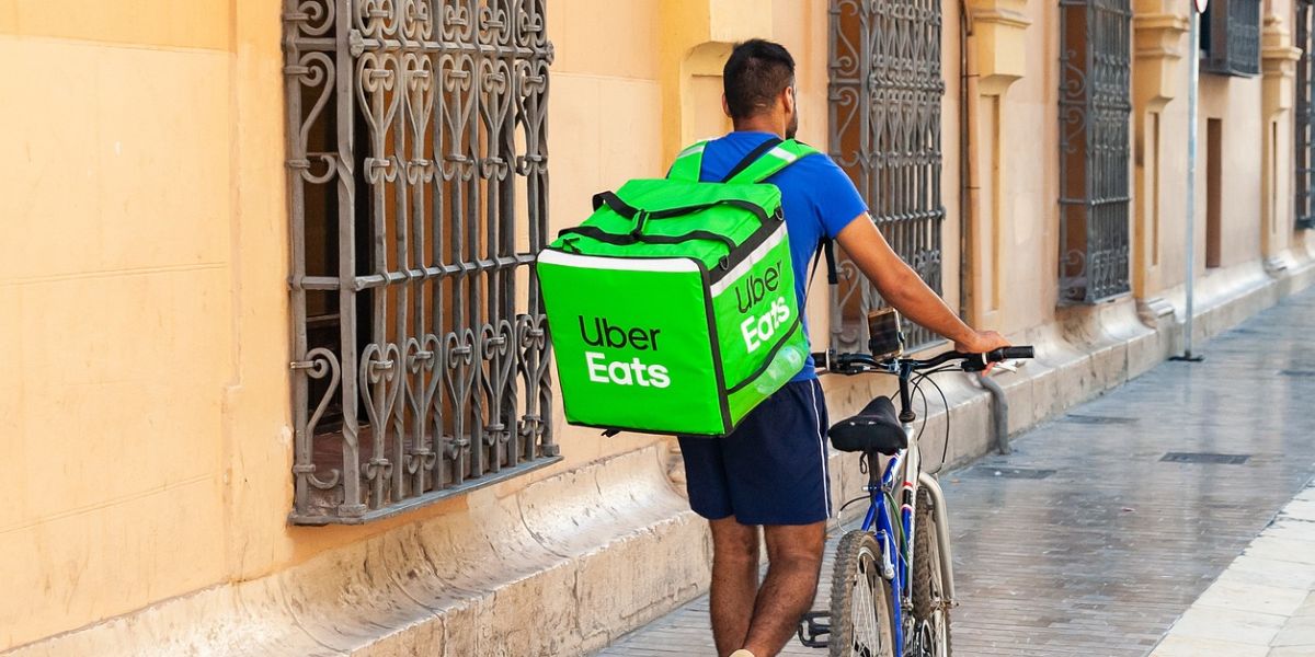 Entregador do Uber Eats caminhando com bicicleta ao lado em uma rua lateral