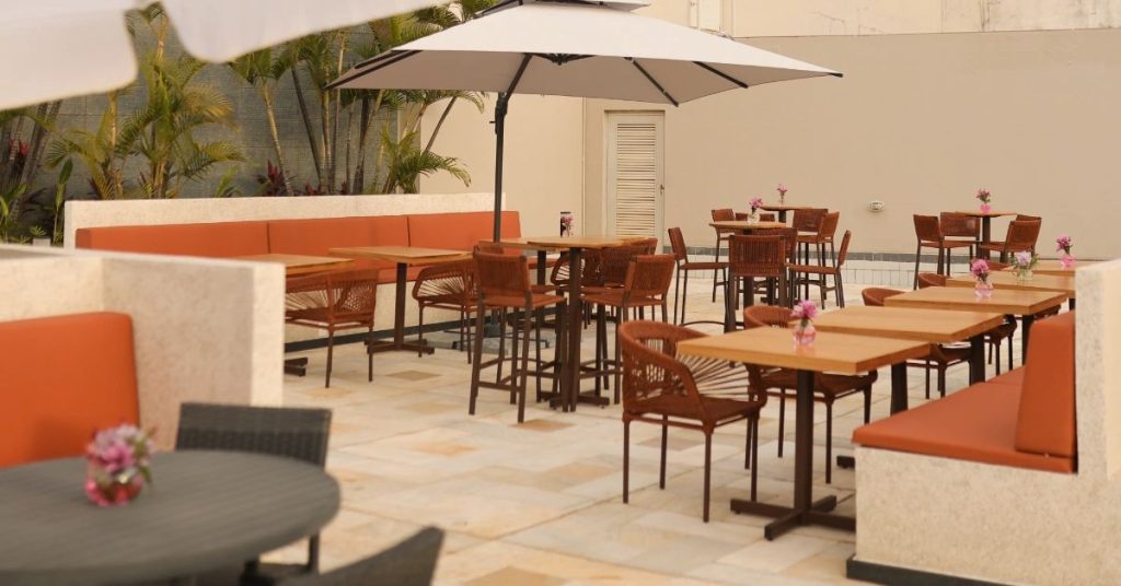 Espaço ao ar livre decorado com poltronas laranja e mesas de madeira em um pátio moderno.