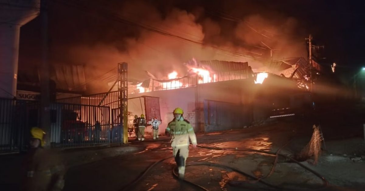 Incêndio de grandes proporções atinge fábrica da Suggar no bairro Pilar, em Belo Horizonte, durante a madrugada, com chamas e fumaça saindo do telhado enquanto bombeiros atuam no combate ao fogo.