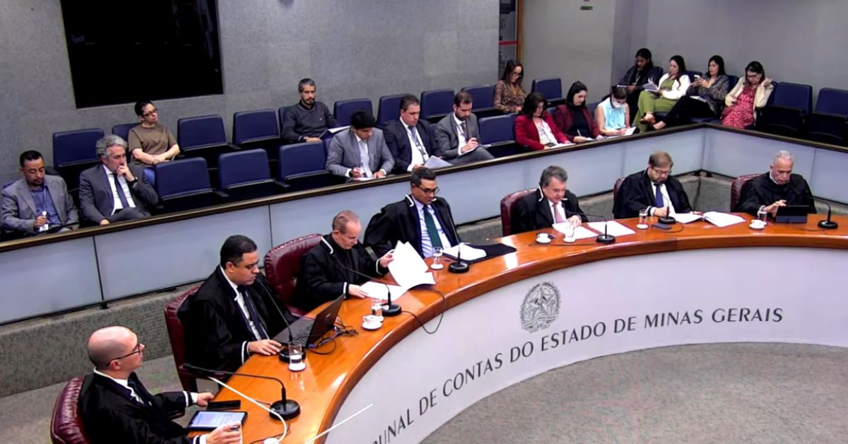 Sessão plenária do Tribunal de Contas do Estado de Minas Gerais (TCE-MG), com conselheiros reunidos em torno da mesa principal durante julgamento. Ao fundo, servidores, advogados e demais participantes acompanham a reunião nas cadeiras do plenário. Na parte frontal da bancada, aparece a identificação do Tribunal de Contas do Estado de Minas Gerais.