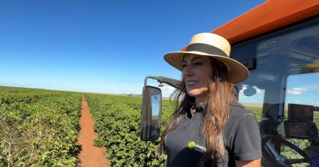 Imagem mostra mulher em cima de um tratô, em uma plantação de café
