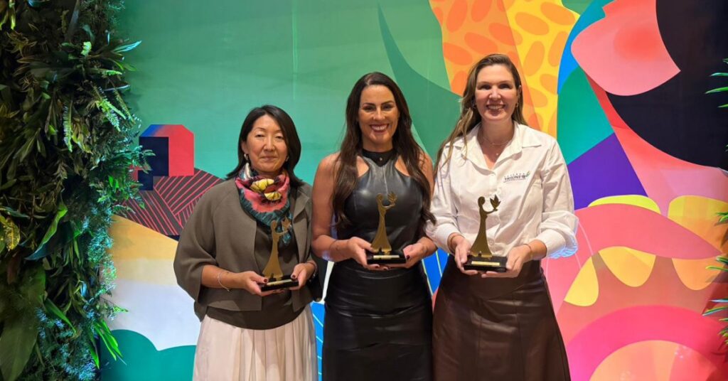 Imagem mostra três mulheres segurando, cada uma, um troféu