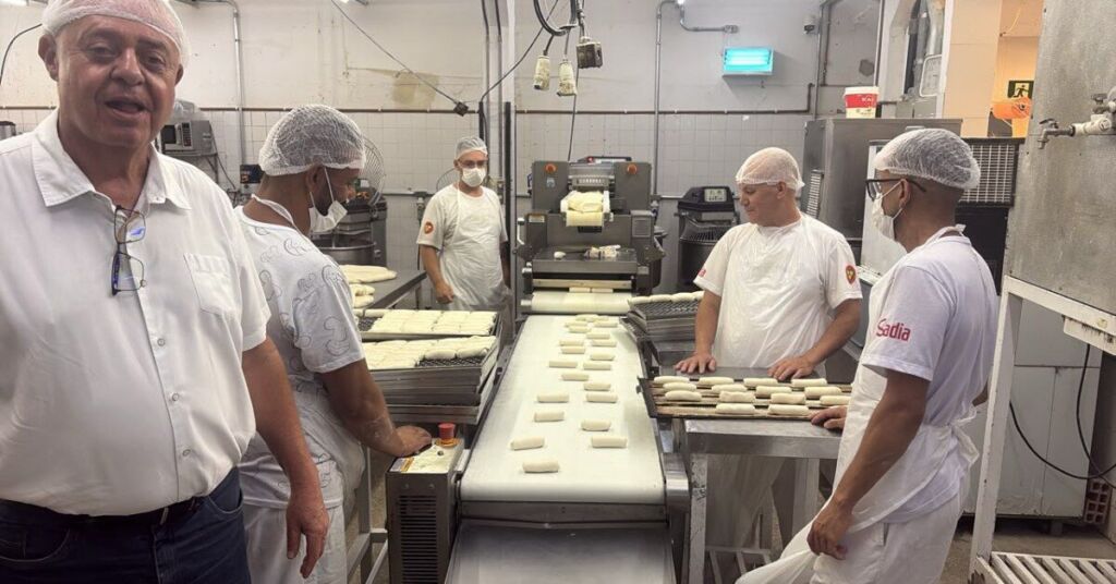 Imagem mostra setor de produção de uma padaria com profissionais trabalhando