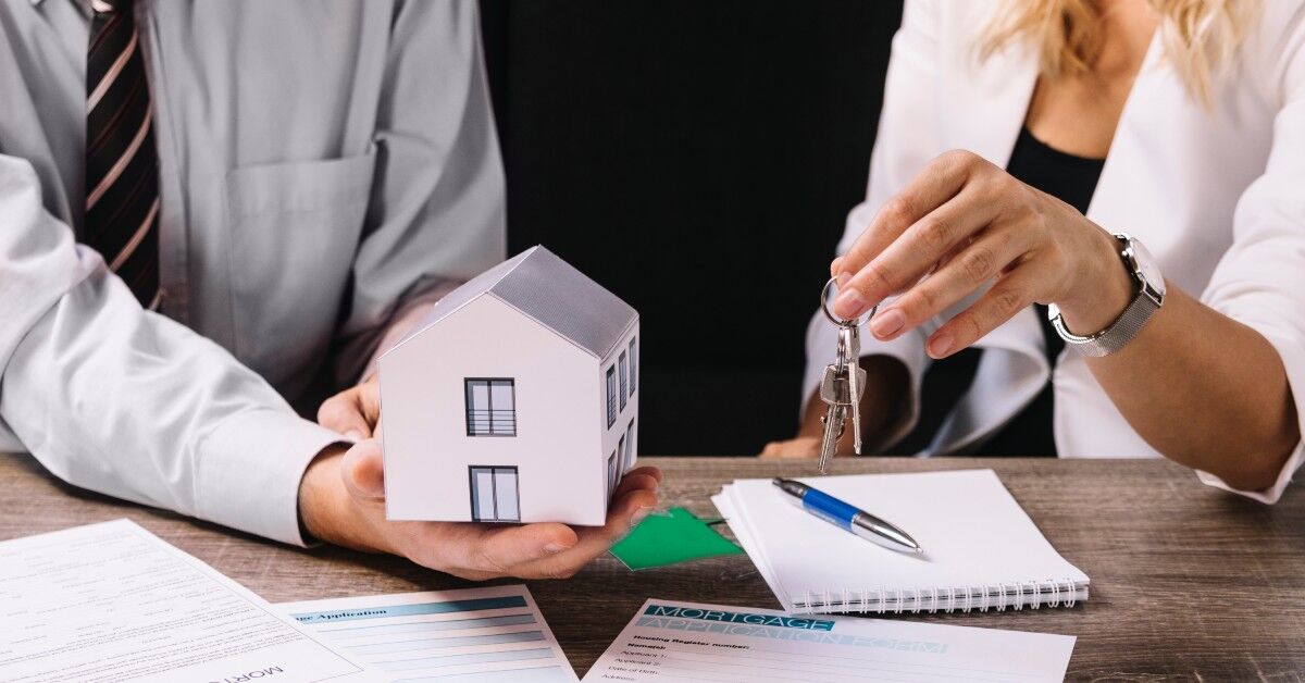 Imagem mostra duas pessoas em uma mesa assinando documentos de um possível contrato de consórcio/aquisição imobiliária