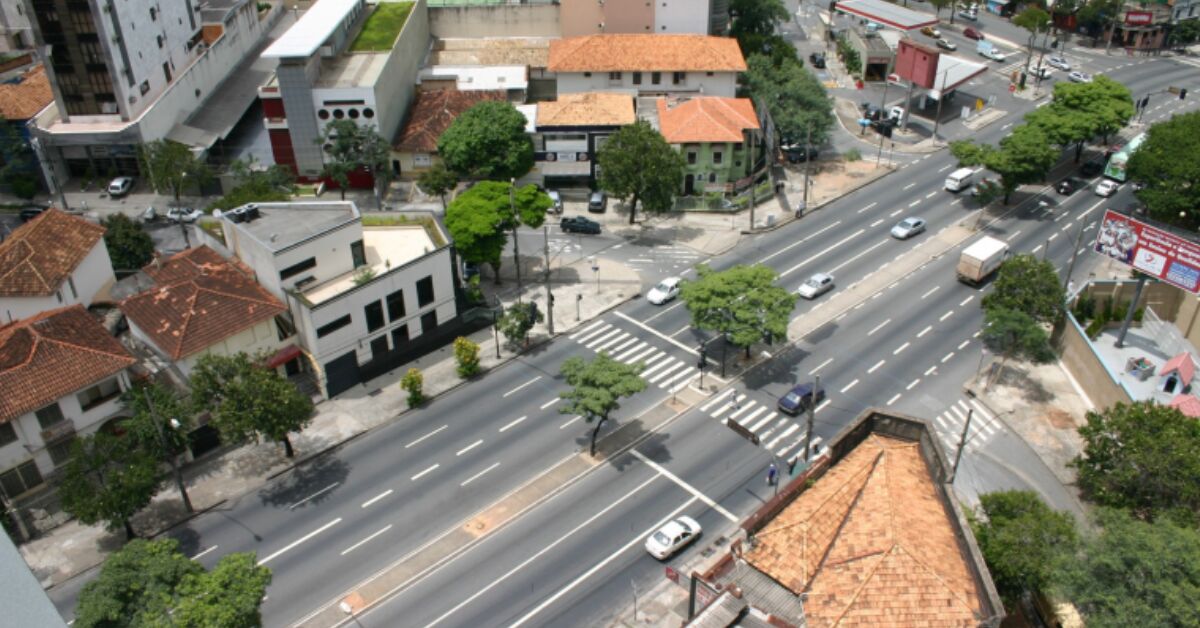 Vista aérea de uma avenida movimentada em uma cidade com casas e prédios ao redor.