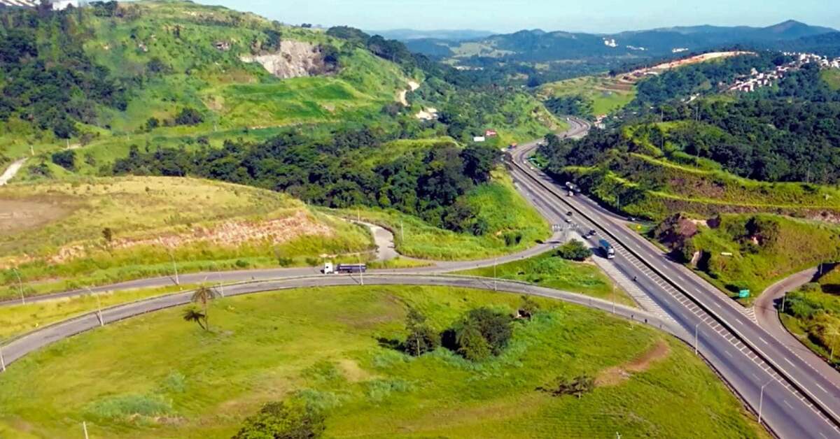 Vista aérea de uma rodovia sinuosa cercada por colinas verdes e vegetação