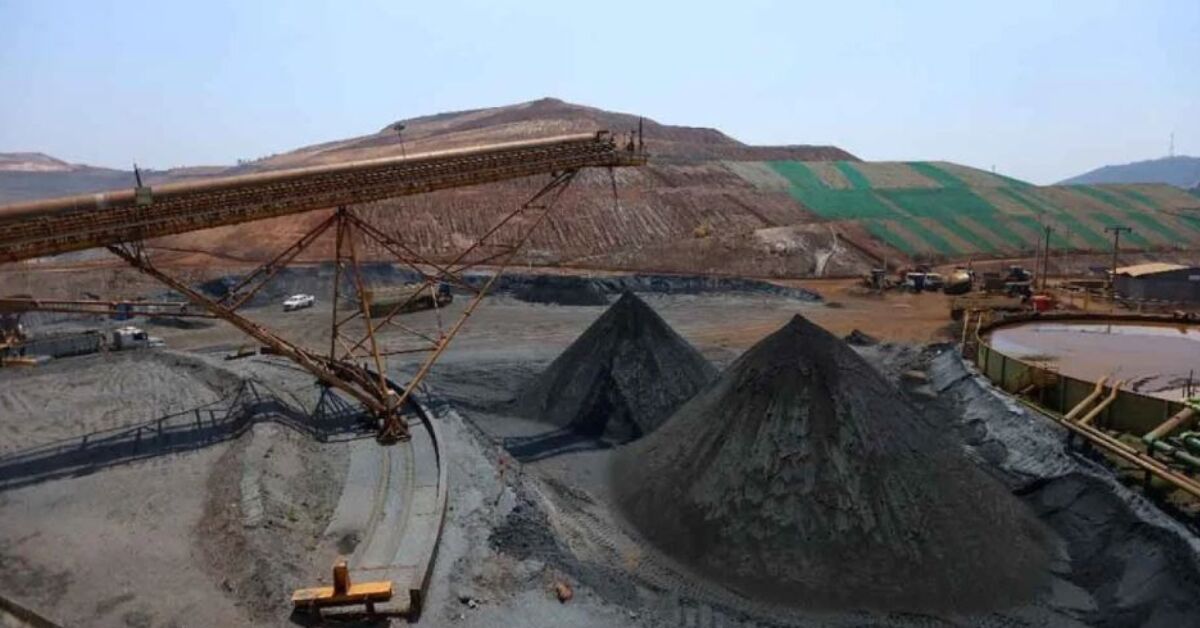 Operação de mineração com correia transportadora e pilhas de minério.